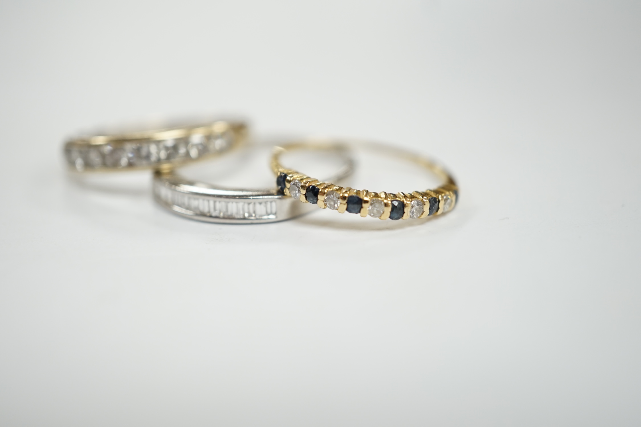 A white metal (stamped 950) and thirteen stone channel set baguette cut diamond ring, size O, together with two other unmarked gem set rings including diamond half eternity ring.